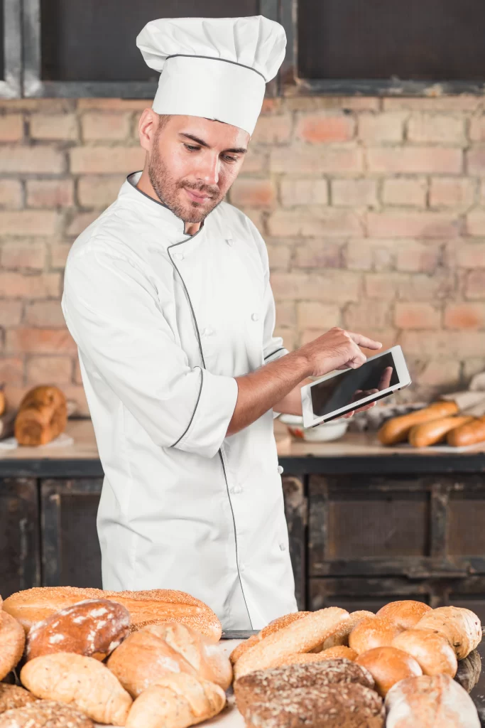 male-baker-looking-assortment-breads-using-digital-tablet